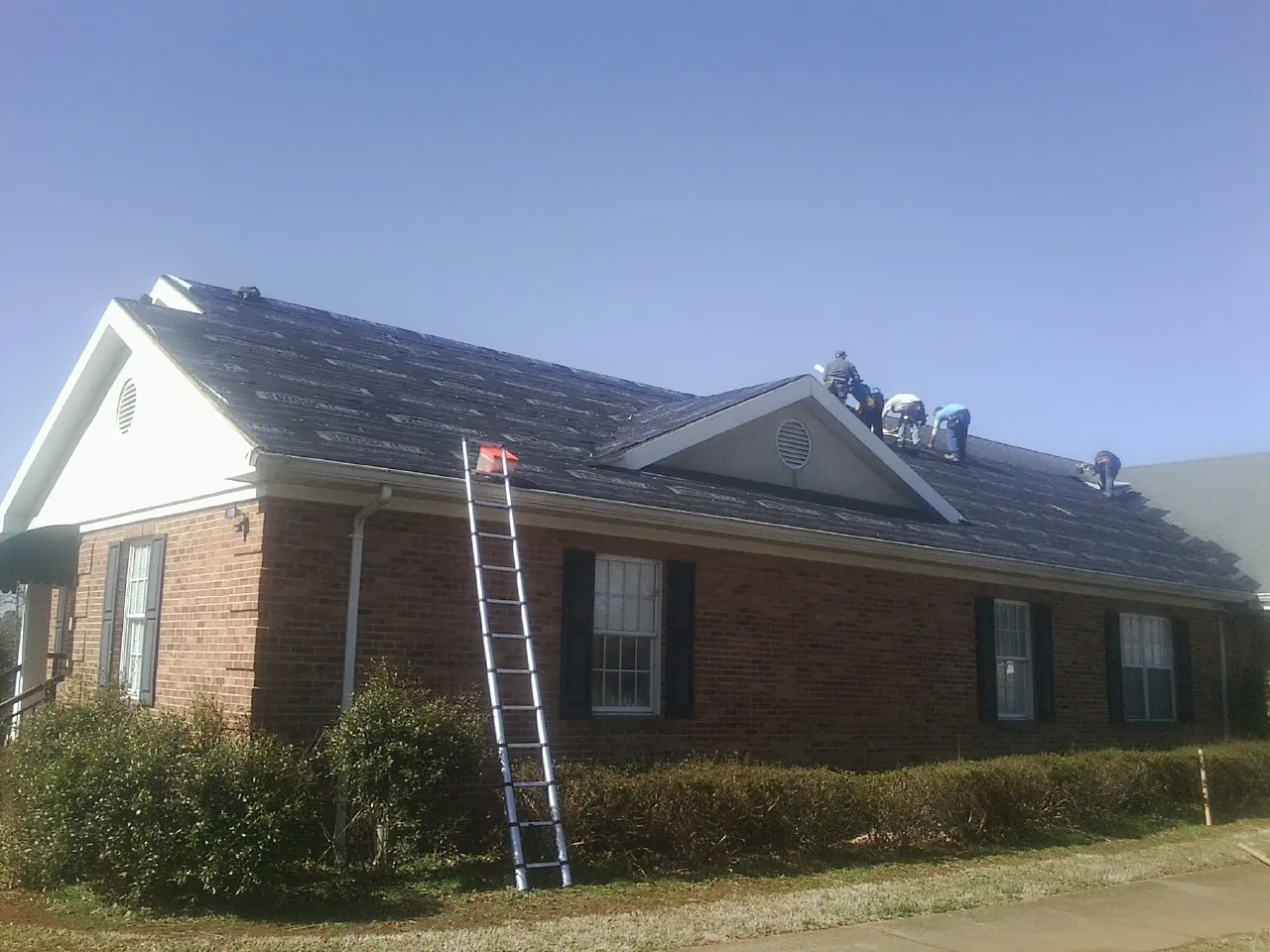 Crew tearing shingles off a brick ranch roof with a ladder set — Emergency Roof Repair work by our crew in Tolono