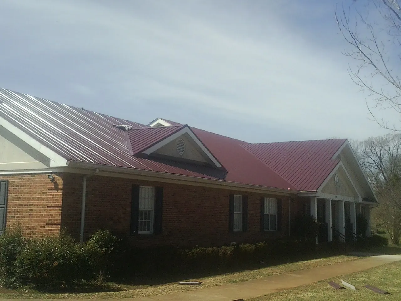 Red metal roof with gabled entries on a long brick building, from a Hail Damage Roof Repair job in Tolono