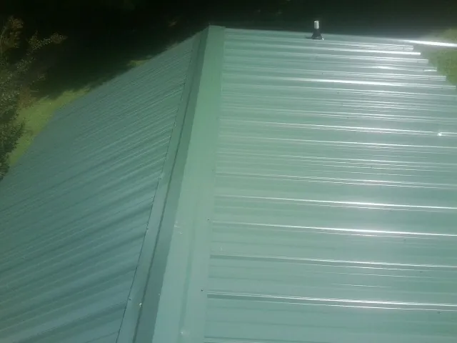 New green metal panels meeting at the ridge of a roof — Flat Roof Repair work by our crew in Tolono