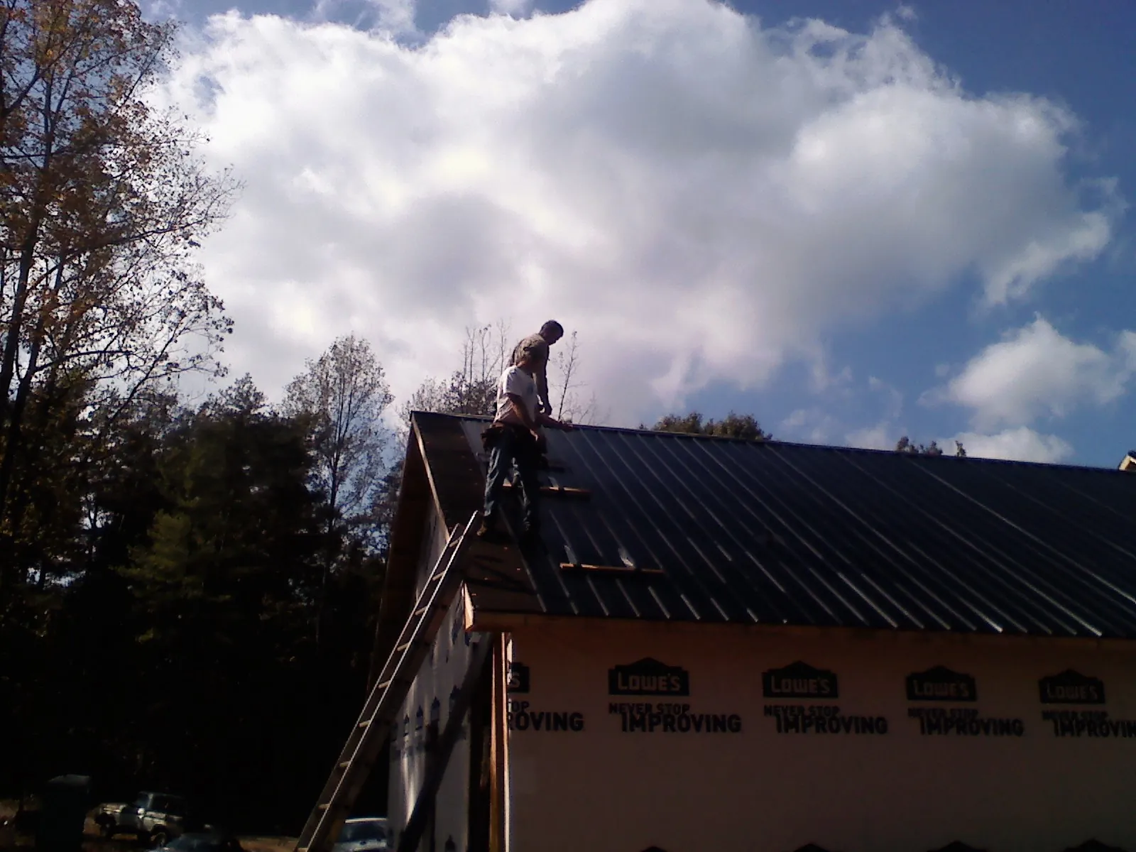 Roofer fastening dark metal panels high against a cloudy sky, from a Roof Inspection job in Tolono