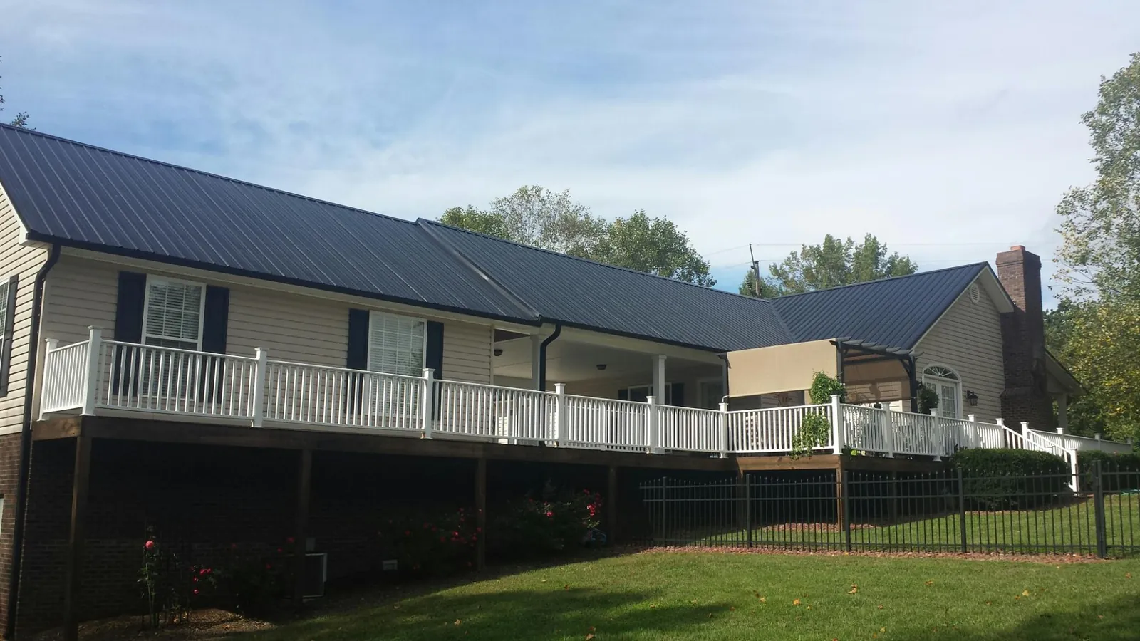 Black metal roof above a long white railed deck on a hillside home in Tolono