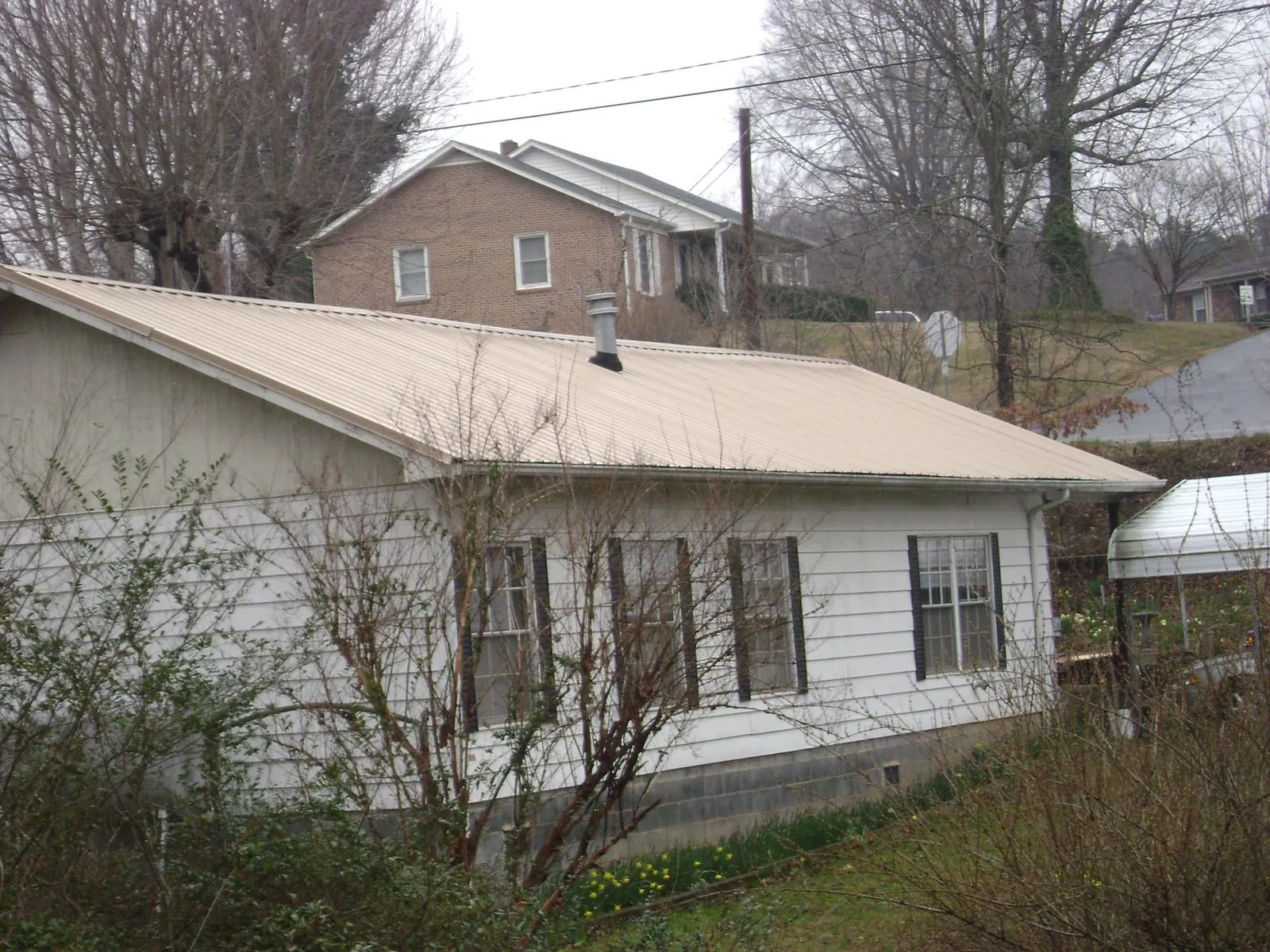 Tan metal roof on a white sided house set into a hillside — Commercial Roofing by Roofing Brothers in Tolono
