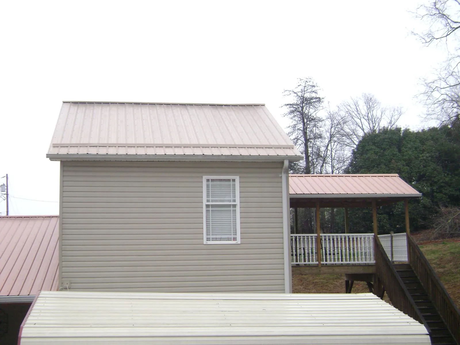Tan metal roofs on a two story addition and attached porch, from a Roof Replacement job in Tolono